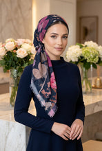 Load image into Gallery viewer, A woman wearing a navy blue long-sleeve dress and a dark floral hijab with pink, purple, and beige butterfly and leaf patterns, standing in a softly lit indoor setting with flower arrangements in the background.