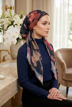Load image into Gallery viewer, A woman wearing a navy blue long-sleeve mock neck top and a dark floral patterned hijab with butterfly motifs, seated in a warm, modern interior setting.
