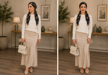 Load image into Gallery viewer, A side-by-side comparison of a woman modeling a two-piece outfit consisting of a white long-sleeve top and a beige satin midi skirt, paired with a navy and gold patterned hijab and holding a cream-colored handbag in a styled indoor room.
